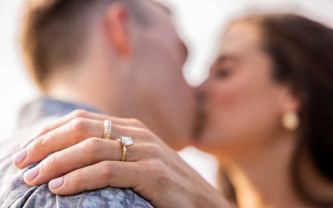 Questions to Ask a Wedding Photographer A close-up of a couple kissing, with focus on the woman's hand resting on the man's shoulder, showing an engagement ring and wedding band.