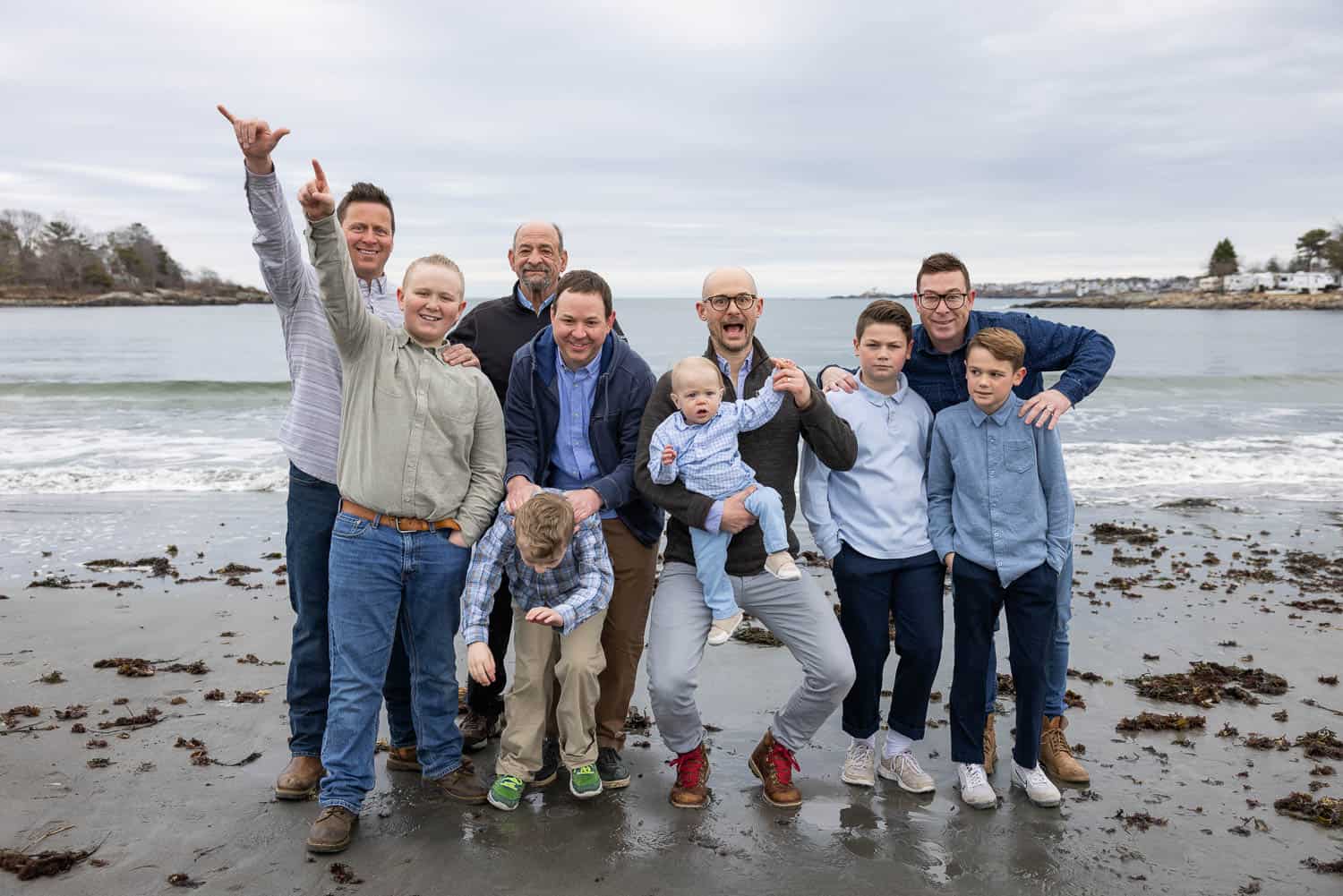A group of ten people, including several children and adults, stand on a beach near the shoreline, posing for a photo on a cloudy day.