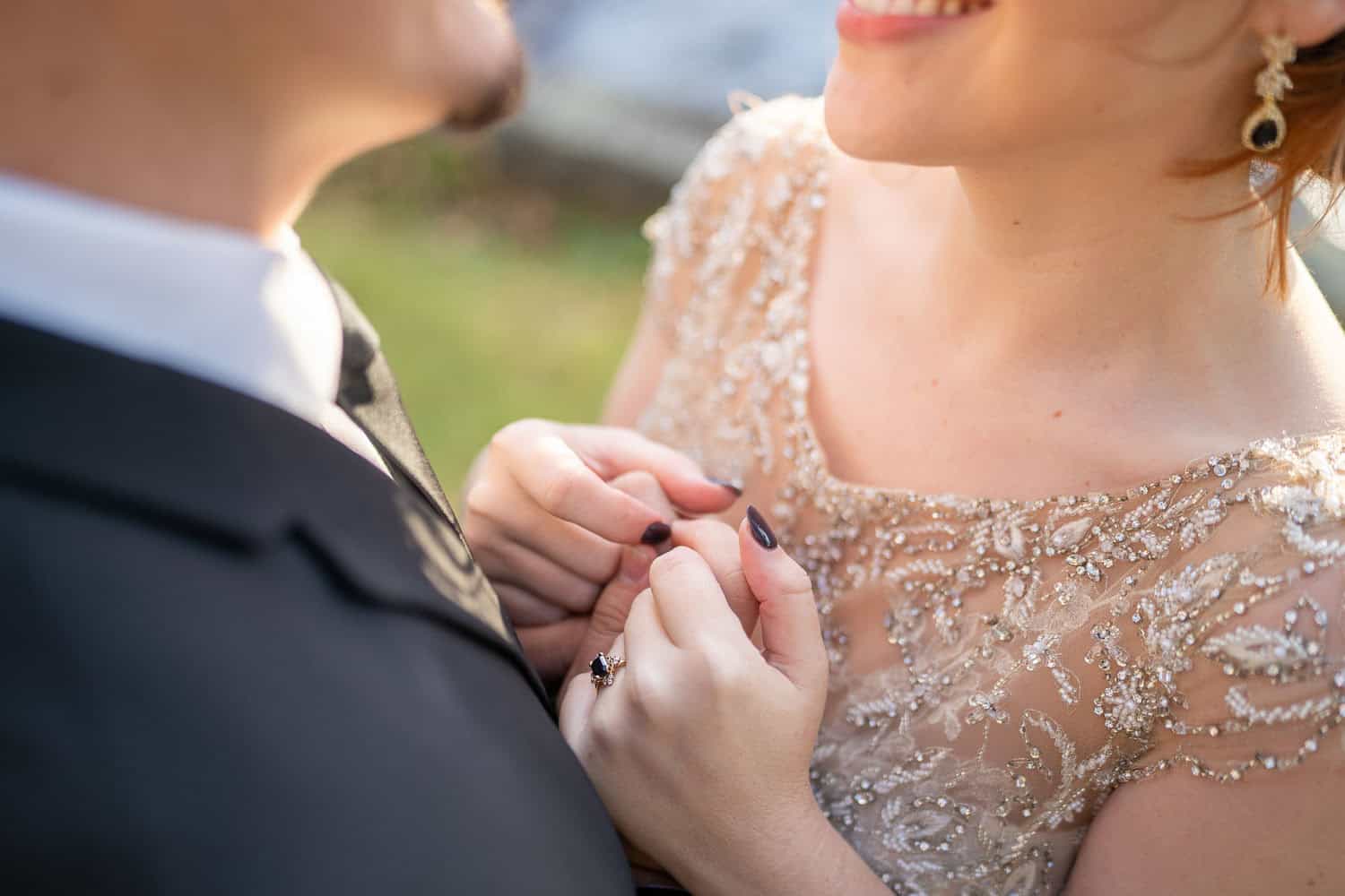 Close-up of a couple holding hands, highlighting the woman's beaded dress, earrings, and smile in an intimate moment.