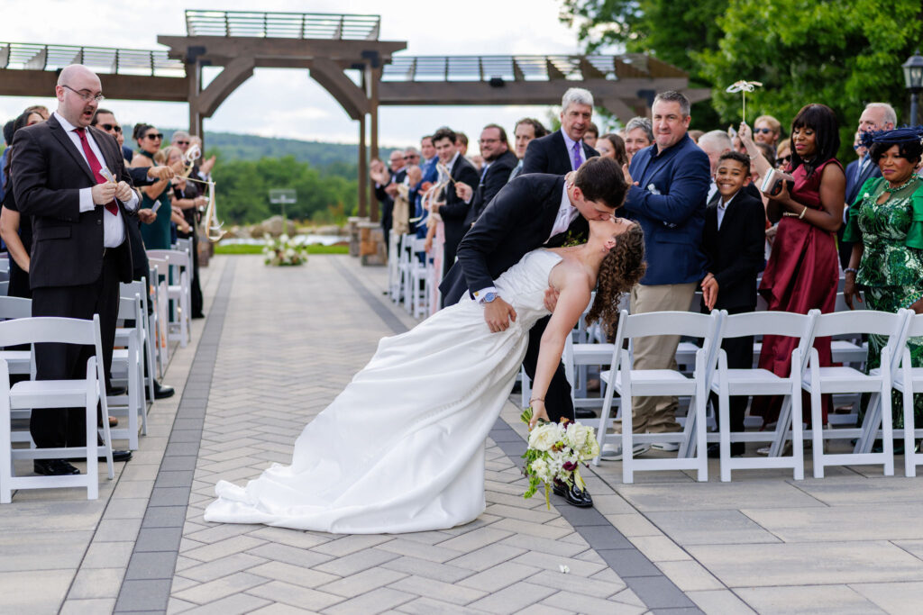 Life in Focus Wedding Videographer, bride and groom share a kiss following the ceremony, groom dips bride with guests looking on